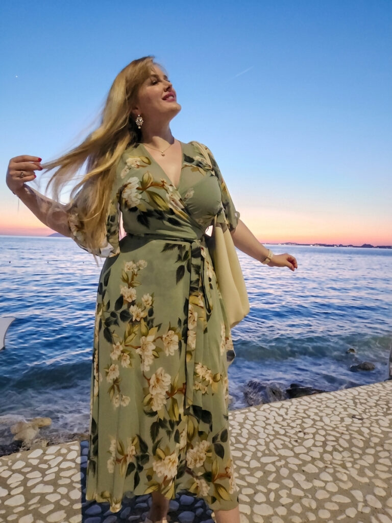 photo of attractive blonde woman with blue eyes in front of a sunset by the ionian sea in albania