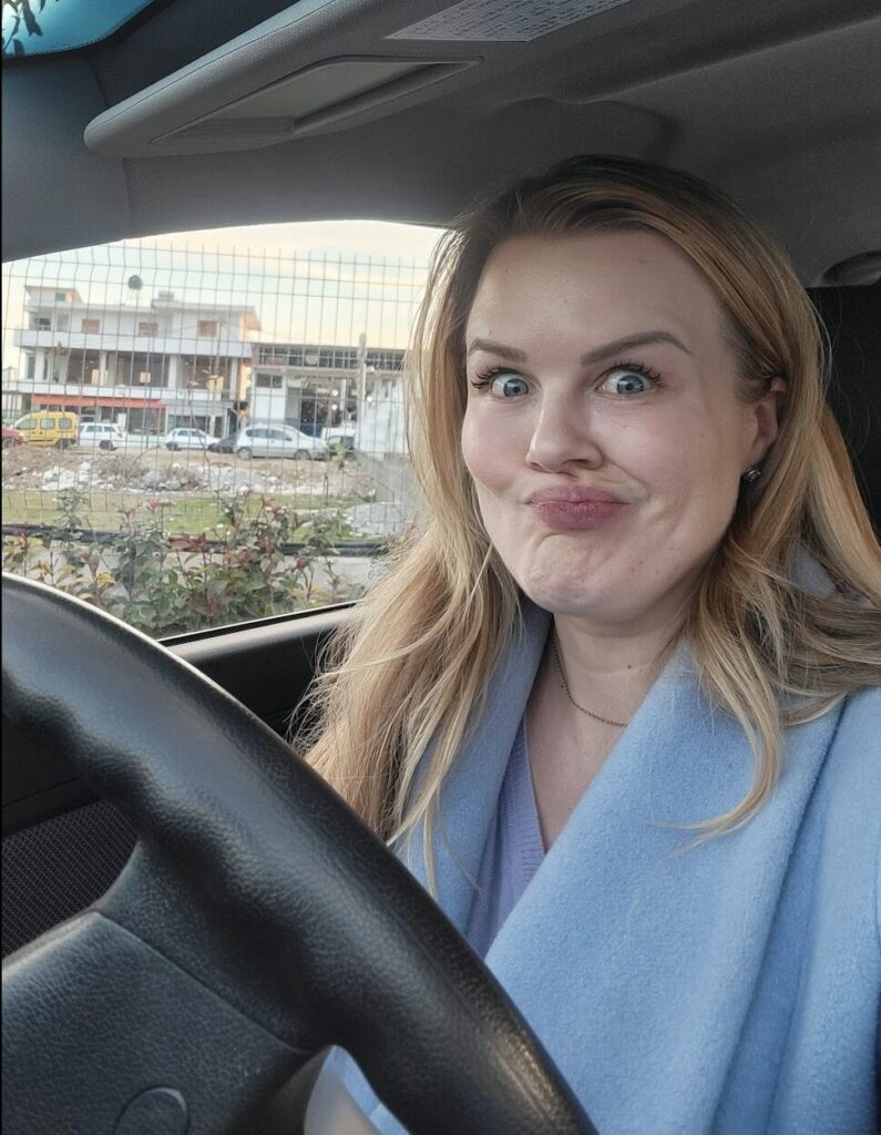 Natalie sitting in a car outside Tirana with an exasperated look on her face