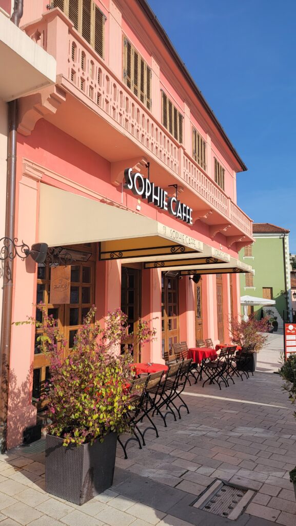 Exterior of Sophie Caffe in a pink building with black metal chairs and red-clothed tables outside.