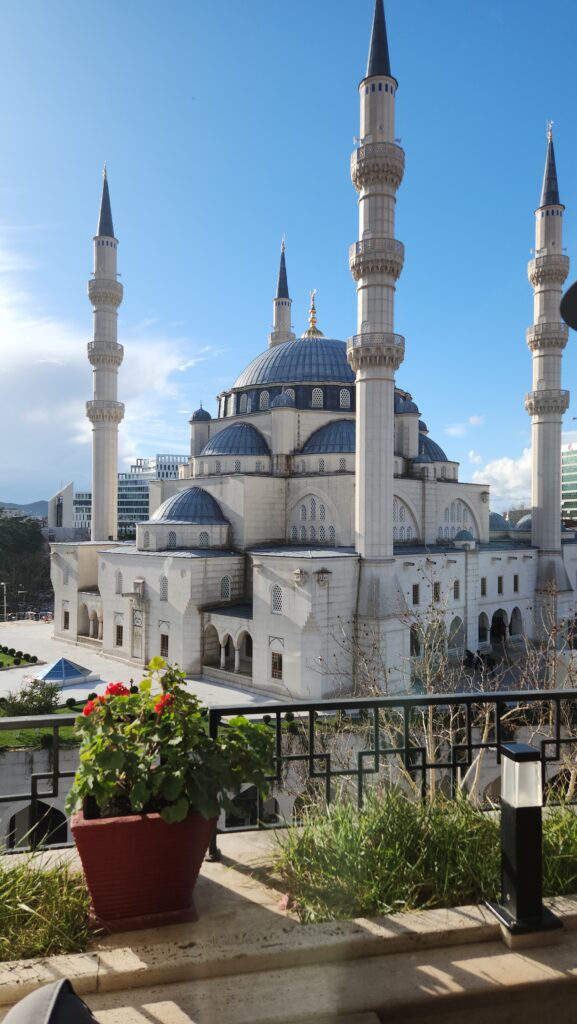 Grand mosque with blue-domed roofs and four tall minarets against a clear blue sky, viewed from a terrace.