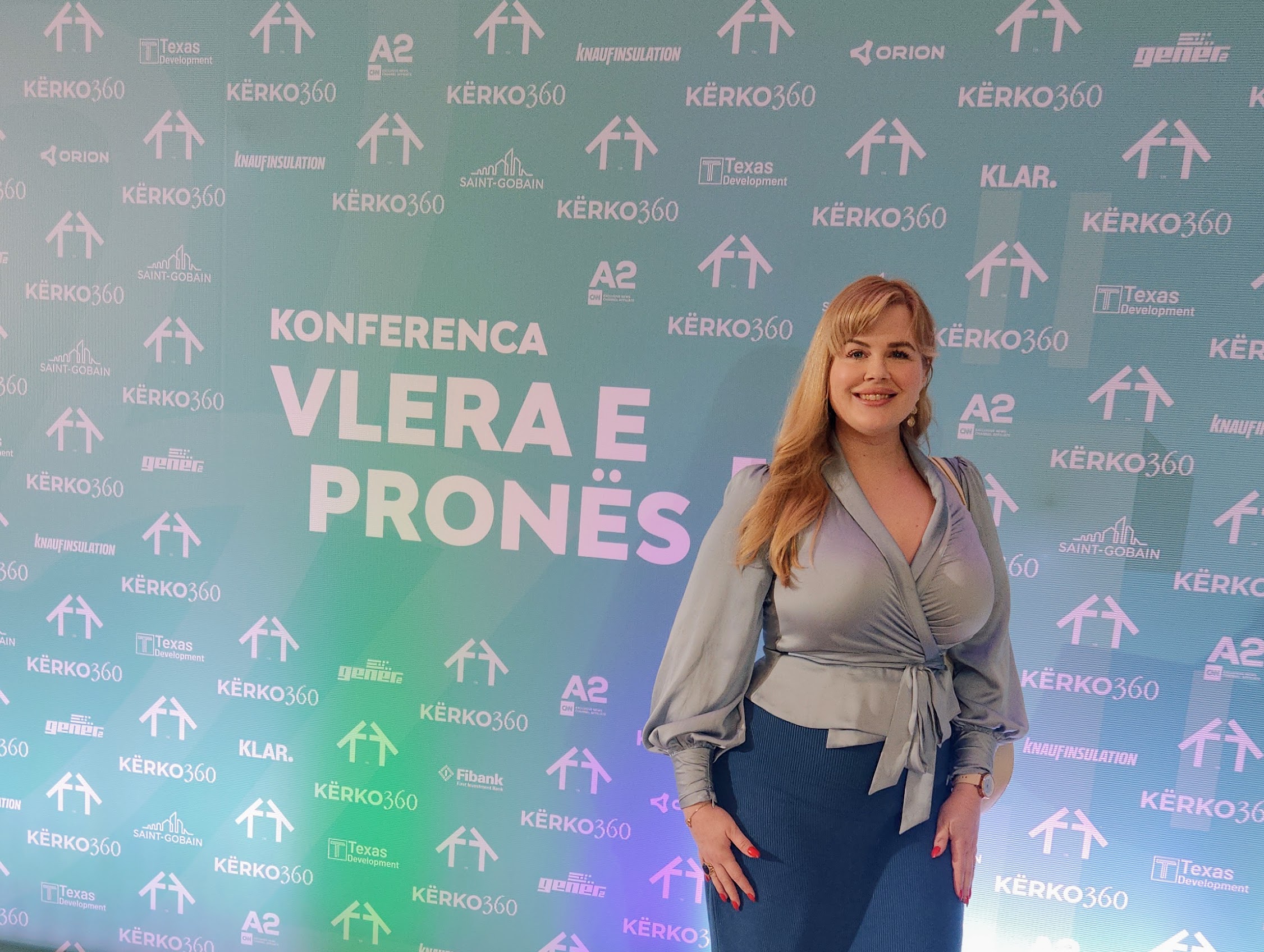 Natalie smiling while posing in front of a professional event backdrop for a real estate conference in Albania.