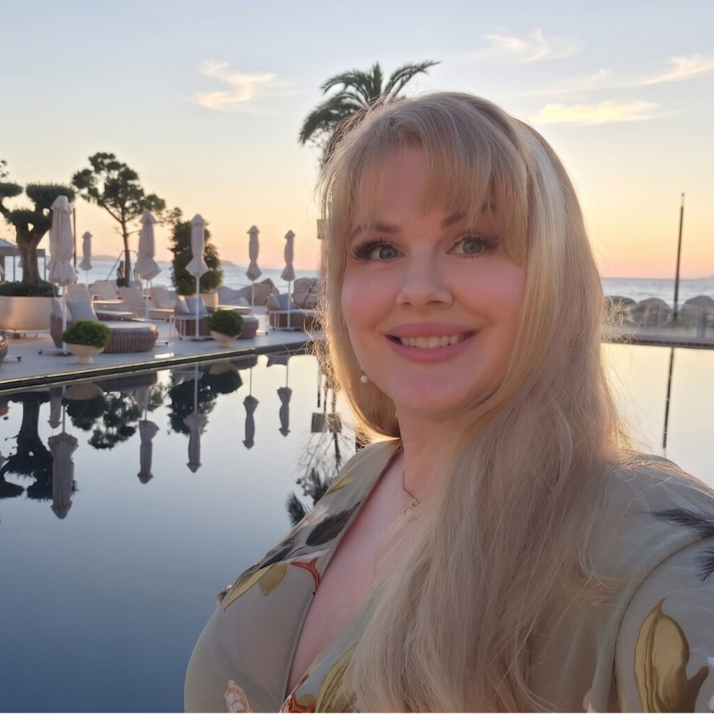 photo of attractive blonde woman with blue eyes in front of a sunset by the ionian sea in albania