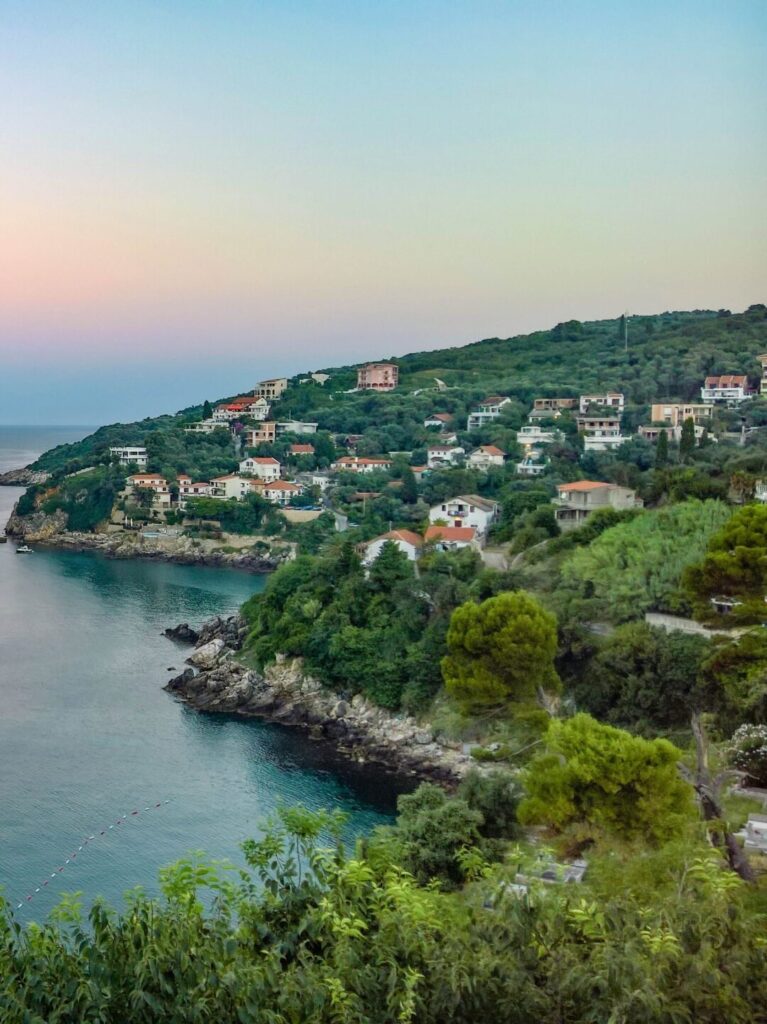 Coastal view of the Albanian Riviera at sunset overlooking a quiet bay and green hillside.
